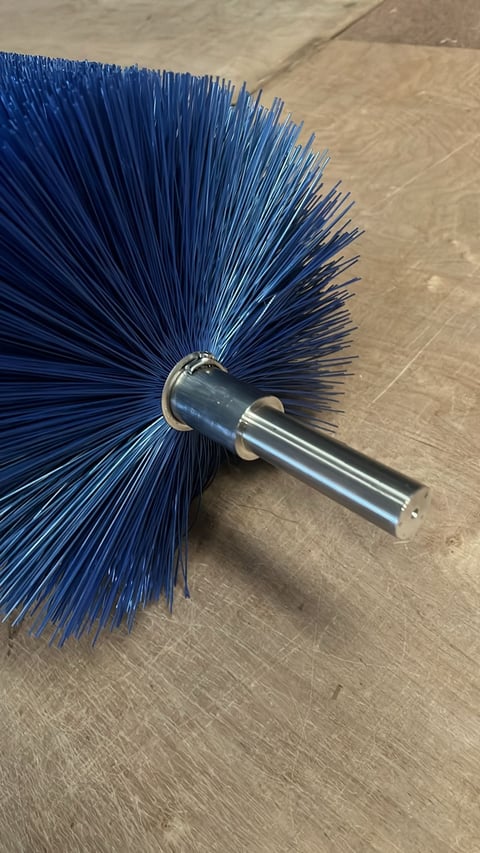 Blue cylindrical brush head with metal shaft on wood-textured surface