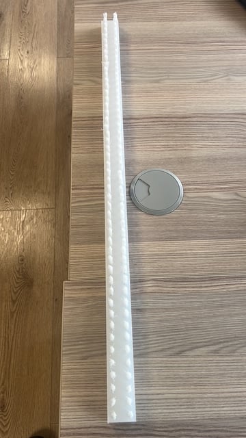 White plastic cable cover on wooden floor next to electrical outlet