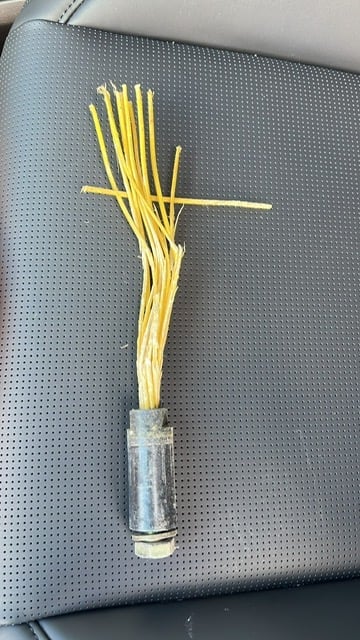 A cross made from yellow straw or raffia attached to a metal tube on a perforated gray pegboard