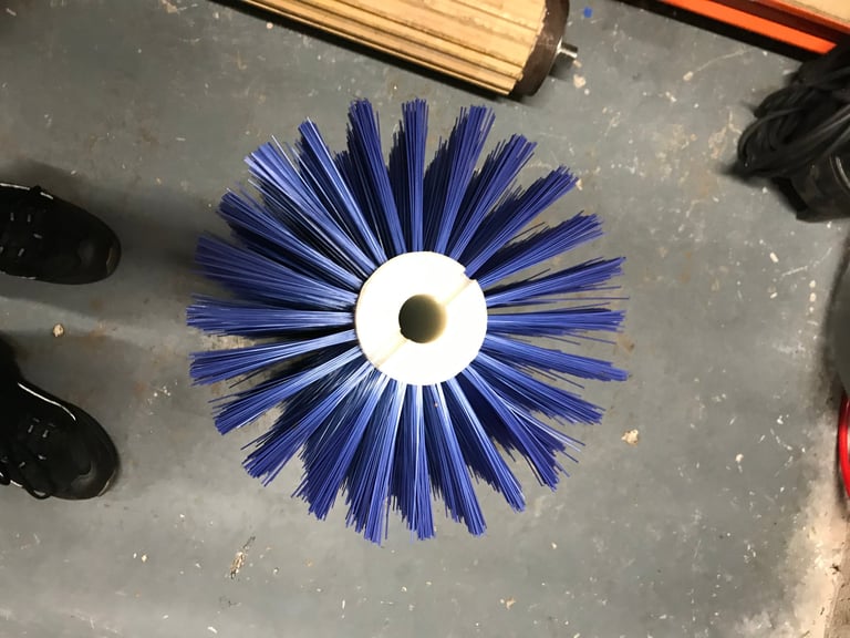 Blue circular brush with bristles radiating outward from white center hub on gray workshop floor