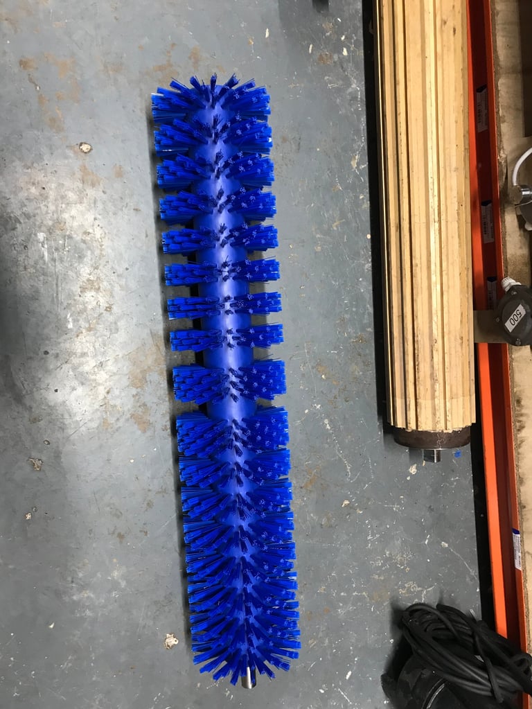 Blue cylindrical pipe brush with bristles laid on a concrete floor next to a wooden frame and tools
