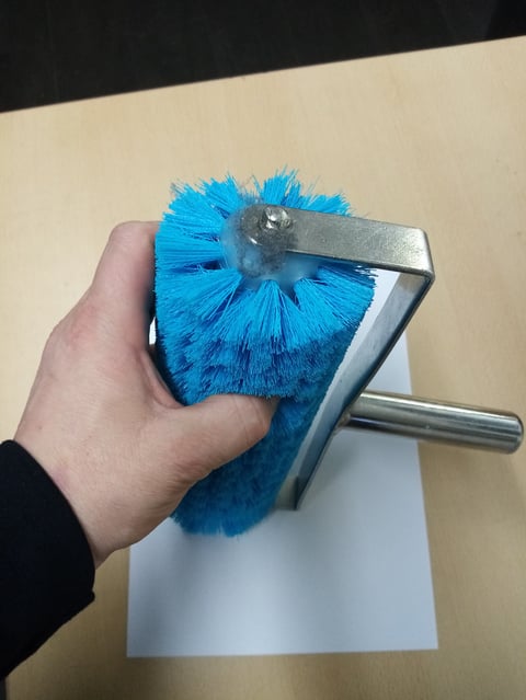 Hand holding a blue circular bristle brush attachment with metal housing and handle