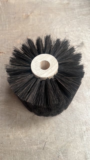 Black synthetic bristle brush head with white plastic center hole, viewed from above on a light surface