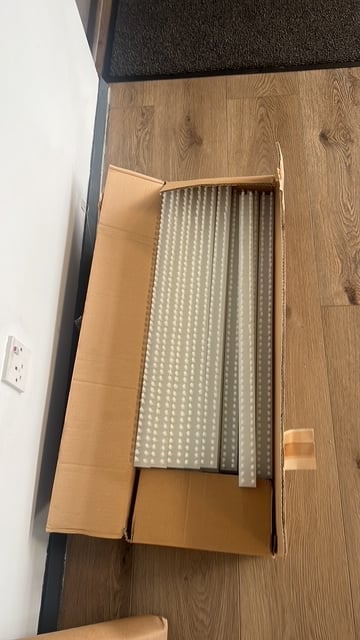 Open cardboard box containing folded bedding and linens on wooden floor