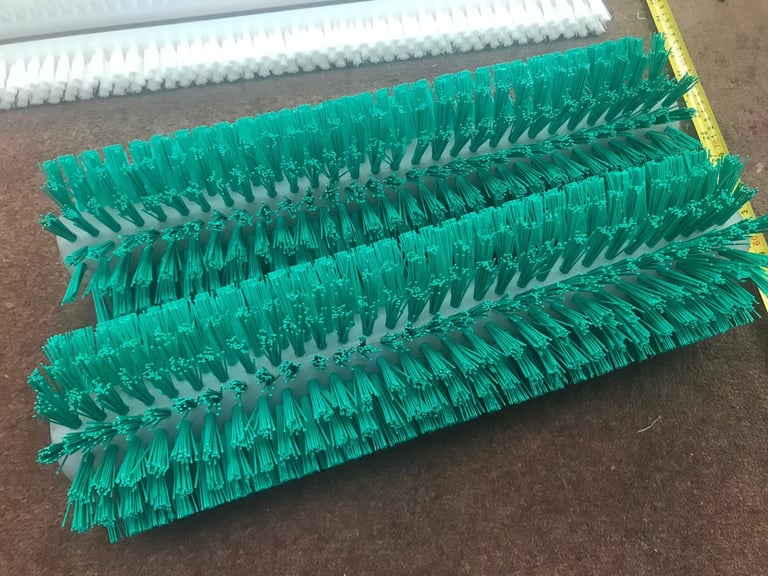 Green cylindrical floor brush with stiff bristles and yellow trim, displayed on concrete surface