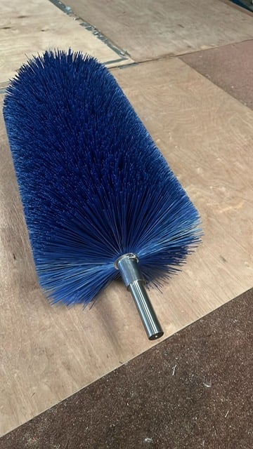 Blue cylindrical floor brush with metal handle resting on a wooden surface outdoors