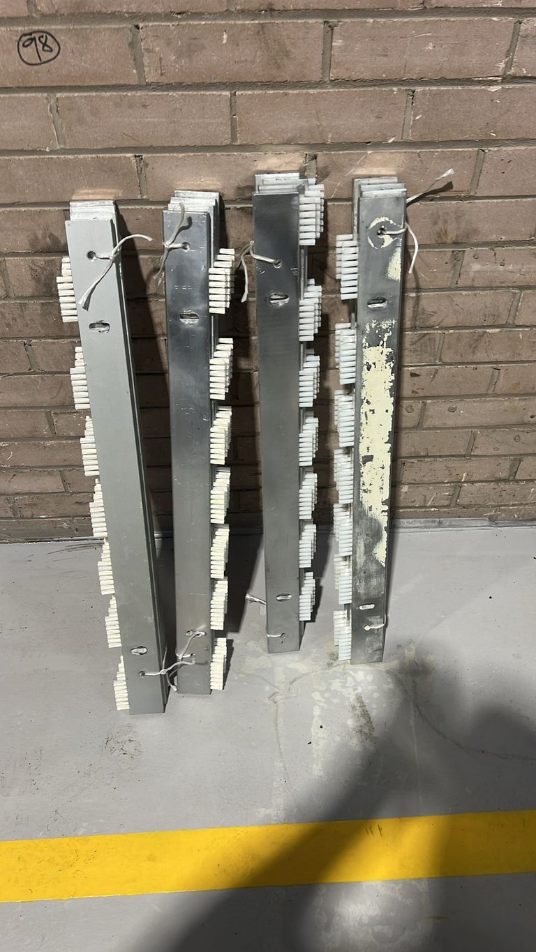 Stack of used metal door frames and panels leaning against brick wall with yellow safety line on floor