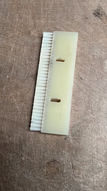 Wooden push stick with white bristle brush attached, featuring two rectangular cutouts, displayed on linen fabric