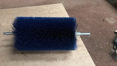 Dark blue cylindrical brush with metal axle resting on a wooden surface