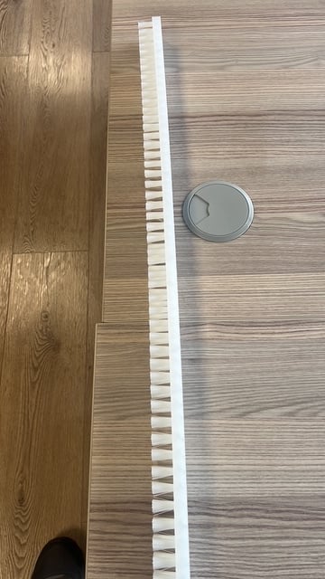 White trim strip and round metal vent on light wood flooring next to darker wood edge
