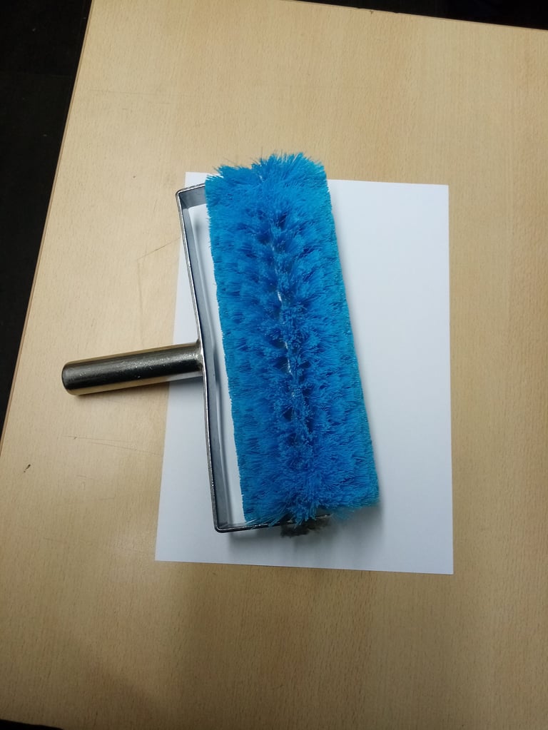 Blue cylindrical paint roller with handle resting on white paper on a wooden surface