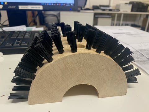 Wooden arch sculpture with black bristles arranged in a fan pattern on an office desk