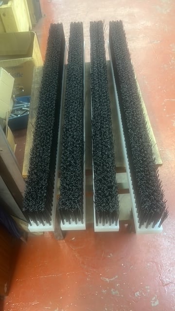 Four black bristle brushes with white handles arranged in parallel rows on an orange floor