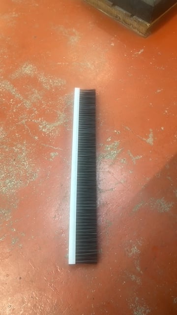 Black ribbed rubber floor squeegee with white handle lying on orange textured surface