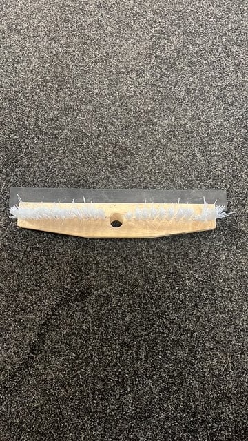 A squeegee with a wooden handle and white rubber blade lying on a dark textured surface