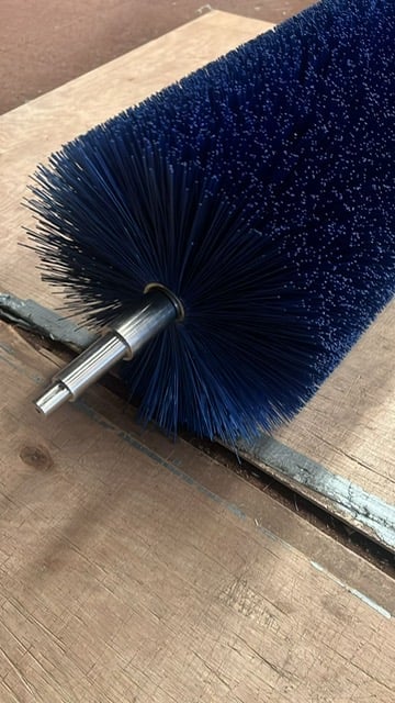 Close-up of a cylindrical brush with dark blue bristles and metal ferrule mounted on a wooden surface