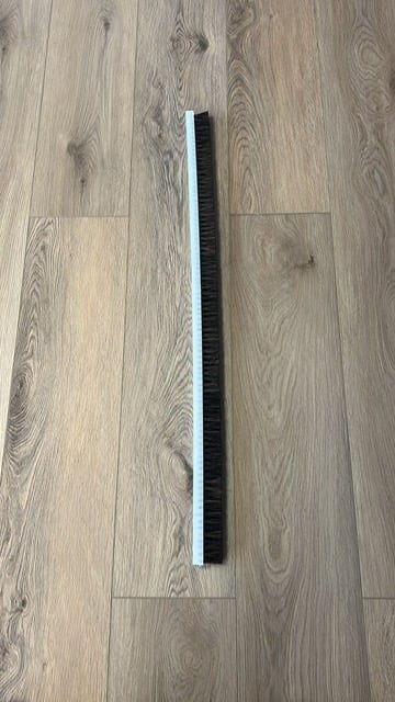 Long black and white brush or scraper tool lying on gray wood plank flooring