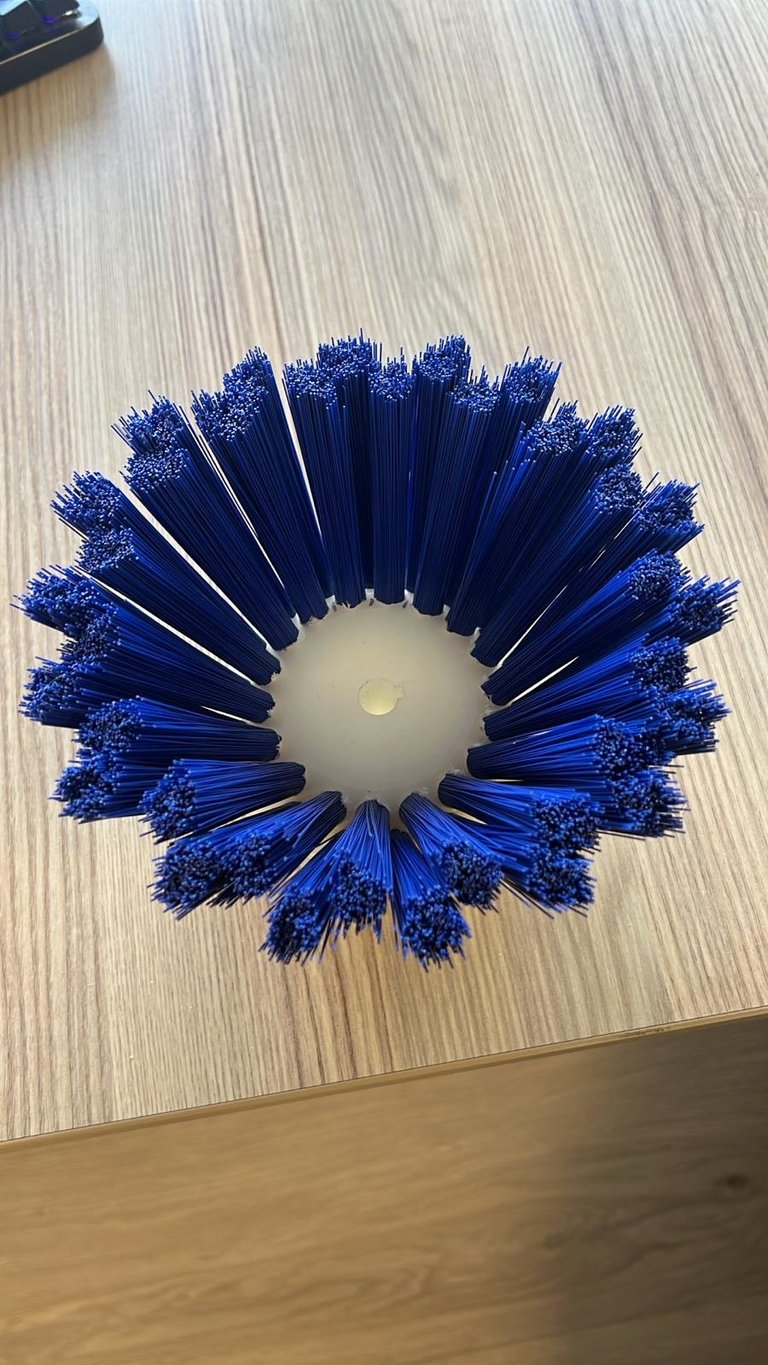 Blue circular brush head with bristles arranged in a radial pattern, viewed from above on a wood-textured surface