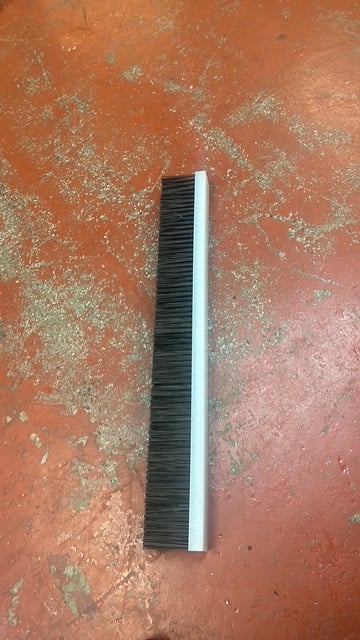 Black and white push broom lying on a terracotta tiled floor with dust and debris
