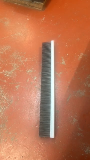 Broom with black bristles and white handle lying on orange textured surface