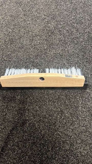 Wooden-handled push broom with white bristles on a dark textured floor surface