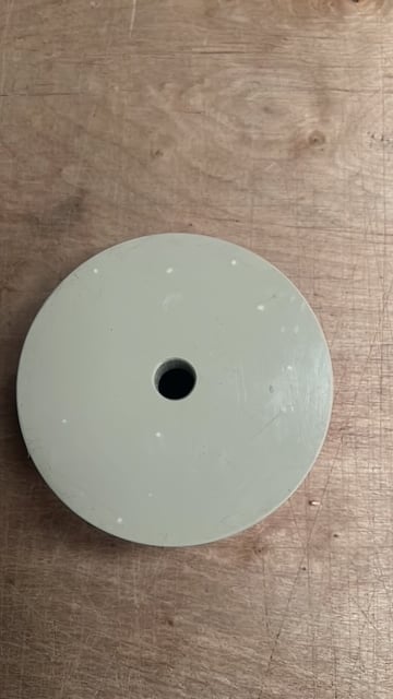 White ceiling medallion or escutcheon with central hole on wooden surface