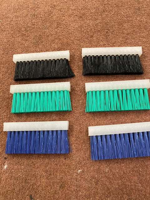 Six replacement brush heads with black, green, and blue bristles arranged in three rows on a cork surface