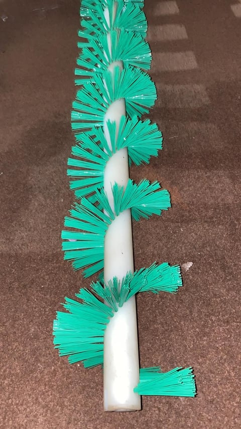 Close-up of a cylindrical brush with a white handle and turquoise bristles arranged in fan-like clusters along its length