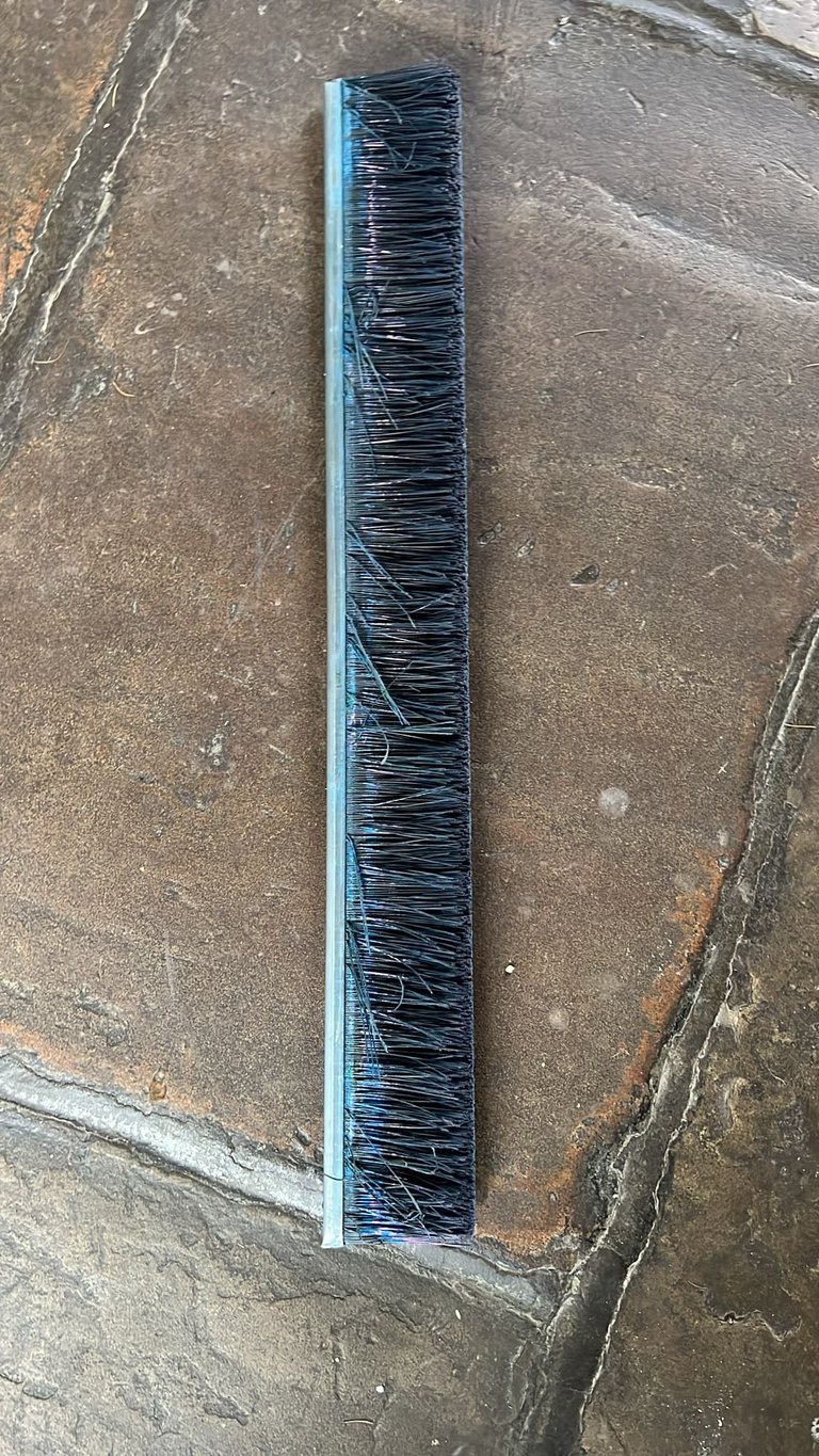 Long-handled push broom with blue handle and black bristles lying on concrete ground
