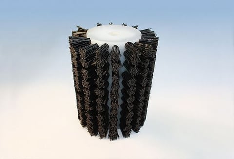 Cylindrical industrial brush with dark bristles radiating outward and white center cap against light sky background