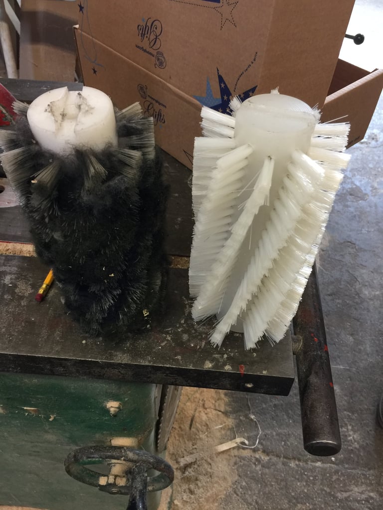 Two cylindrical cleaning brushes, one black and one white, with bristles radiating outward, displayed on a work table