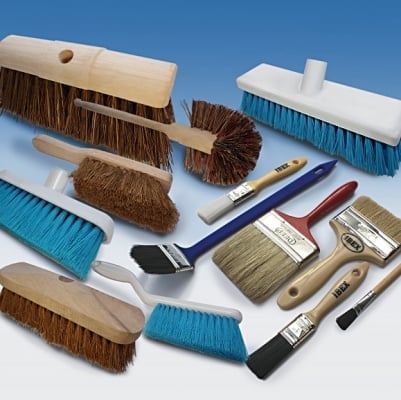 Collection of cleaning brushes and paint brushes in various sizes and styles arranged on white surface against blue background