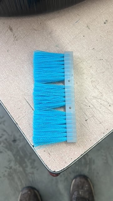 Blue push broom with gray handle on concrete floor, viewed from above
