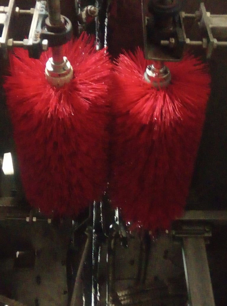 Two red fluffy cylinder brushes mounted on industrial cleaning equipment