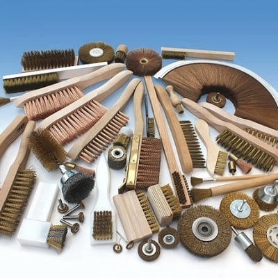 Collection of industrial brushes and wire wheels with various natural bristles and sizes arranged on white background