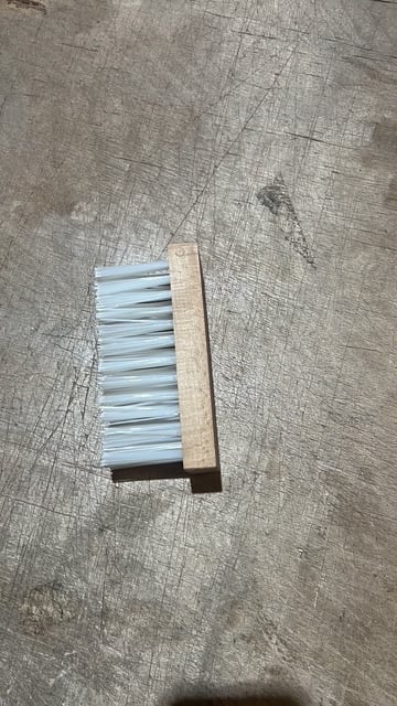 A wooden-handled brush with blue bristles lying on a textured gray surface