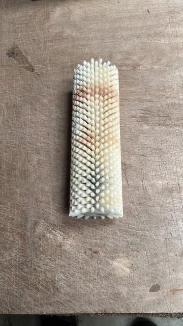 White cylindrical cleaning brush with dense bristles arranged in rows on a beige textured surface