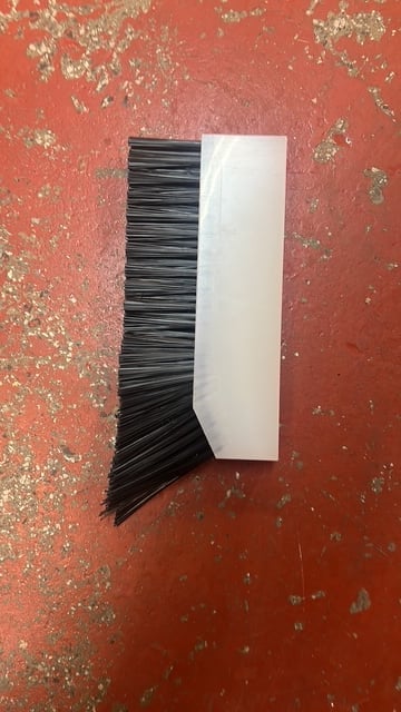 Hand broom with white handle and black bristles resting on a weathered red textured surface