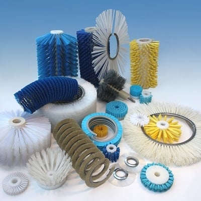 Assorted industrial cleaning brushes and tools in various sizes, shapes, and colors including blue, white, yellow, and tan bristles