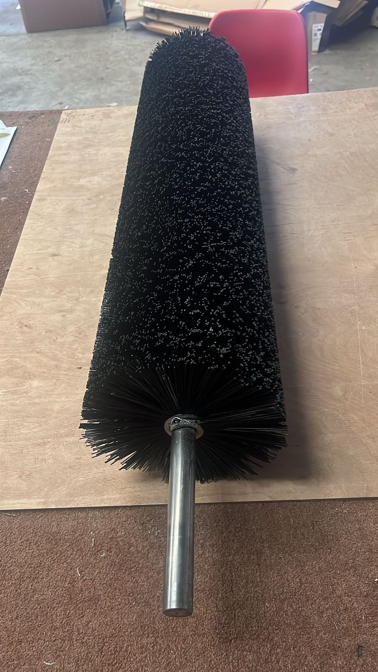 Black cylindrical brush with dense bristles and metal handle lying on wooden surface in workshop
