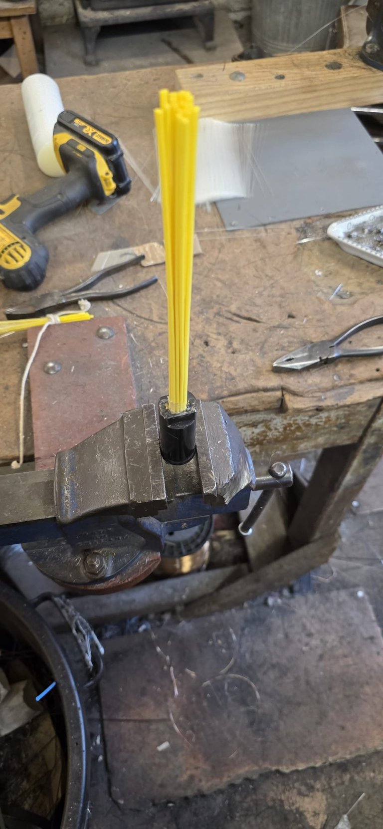 Yellow pencil clamped in a metal vise on a workbench with tools and wood in background