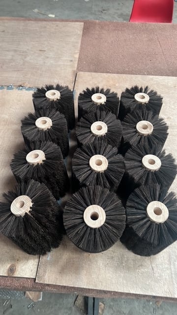 Twelve black cylindrical brush heads with white plastic centers arranged in rows on a wooden surface
