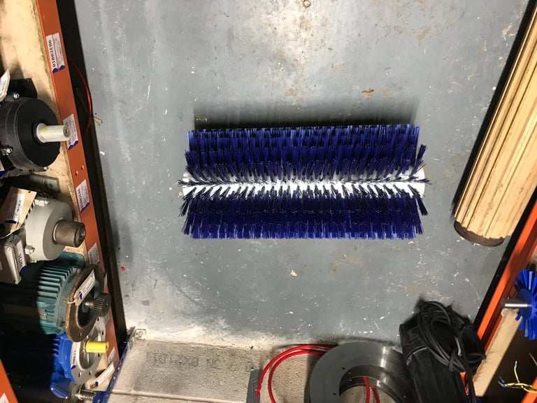 Two rows of blue and white rotating brushes mounted on a gray metal surface in an industrial cleaning equipment