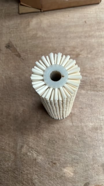 White cylindrical brush filter with light blue center ring and radial bristles arranged in a sunburst pattern on a concrete floor
